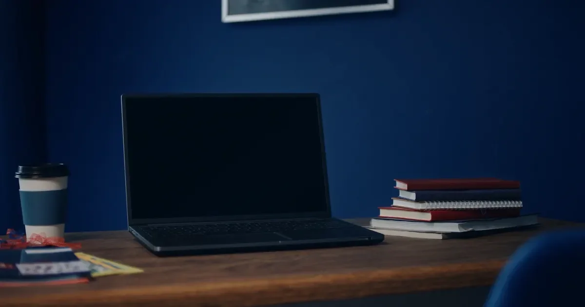 A tidy desk with a laptop, a coffee cup and books against a navy wall