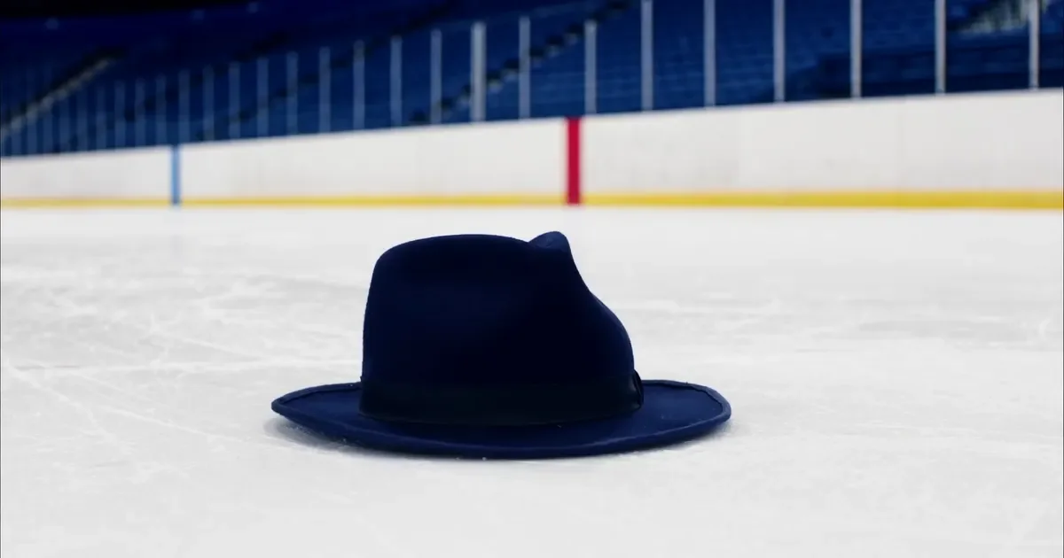 A dark felt hat lying alone on white hockey ice