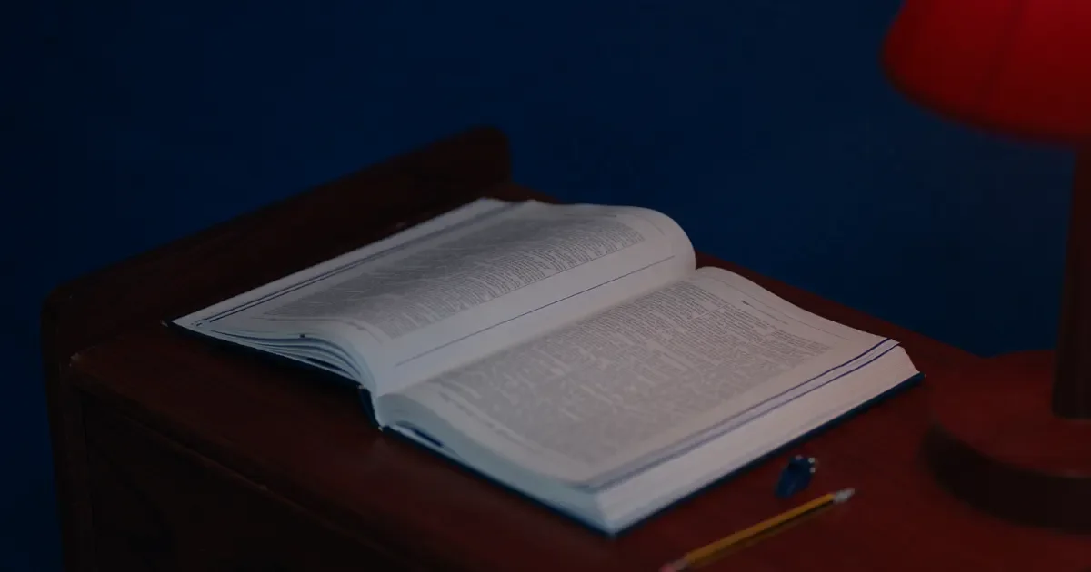 An open rulebook on a wooden desk beside a red lamp