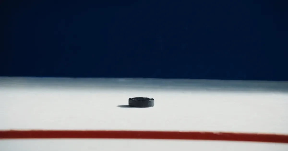 A hockey puck on white ice near a red goal line in an empty arena