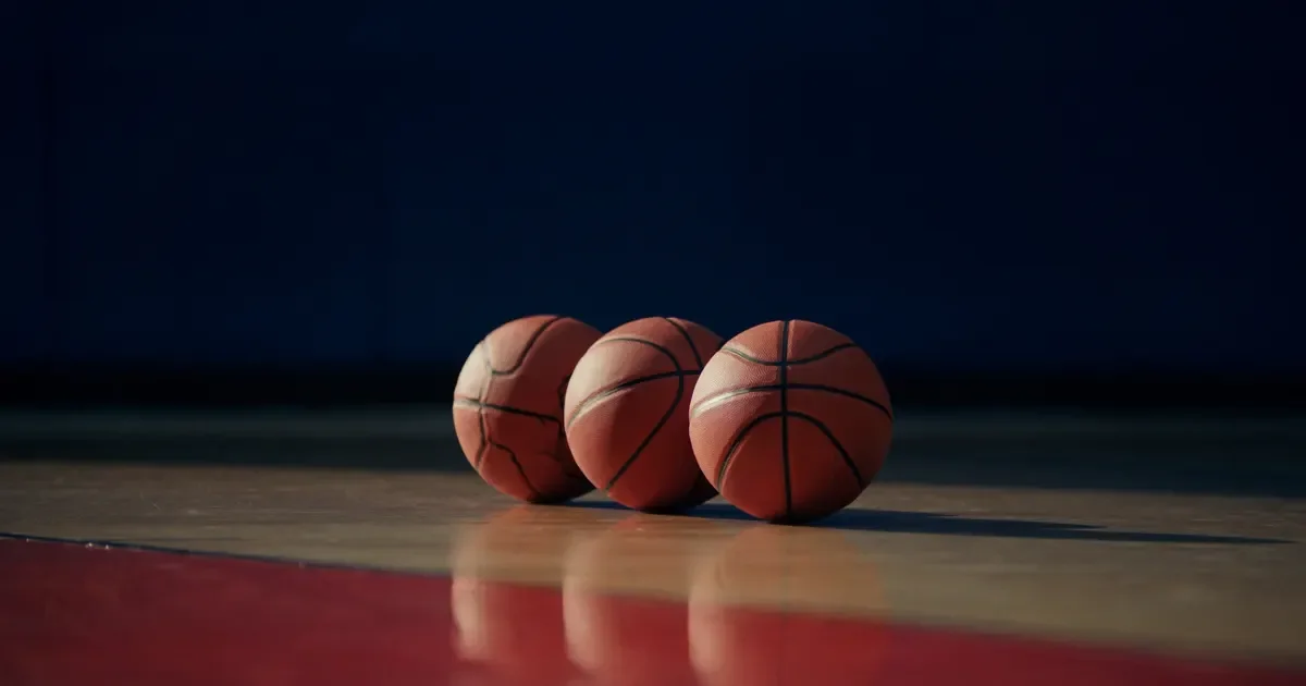 Three basketballs lined up on a polished hardwood court