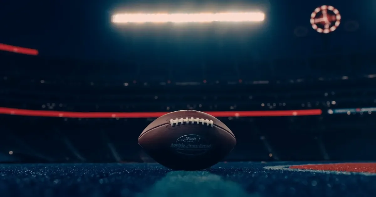 An American football on the turf of an empty stadium under bright floodlights at night