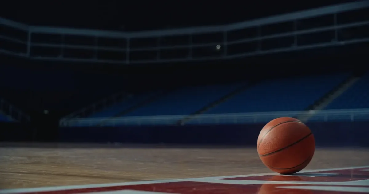 A basketball on a polished hardwood court in an empty arena