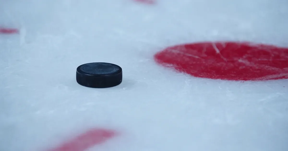 A black hockey puck on white ice beside a red center circle