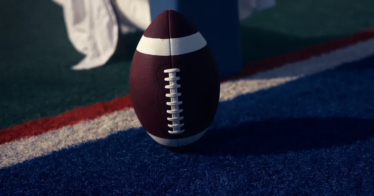 An American football standing on the turf beside a white painted line