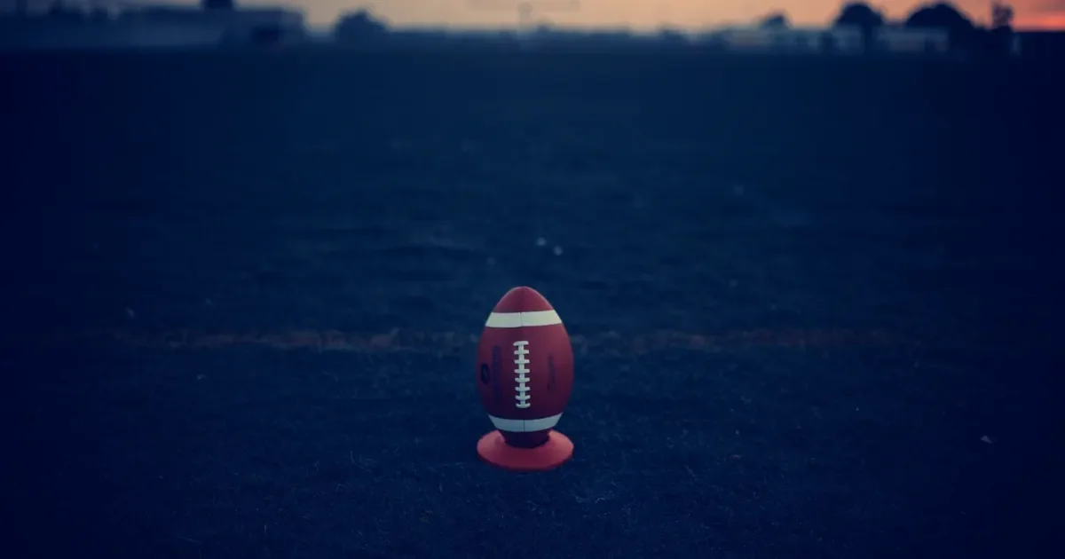 An American football on a kicking tee in an empty field at sunrise