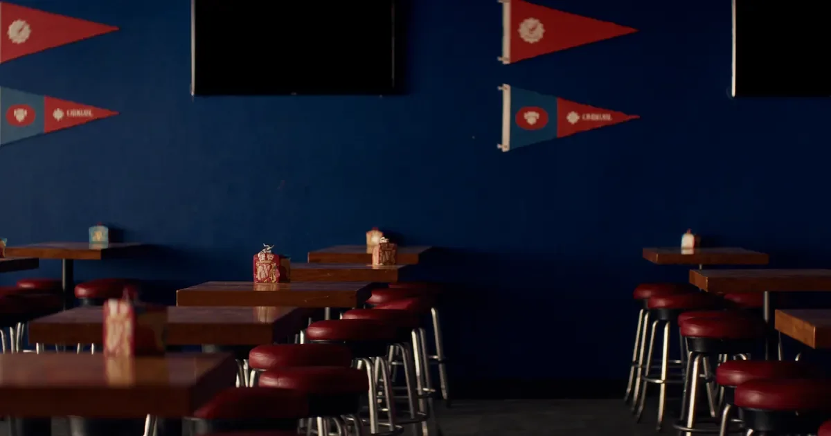 An empty sports bar with wooden tables, red stools and pennants on the wall